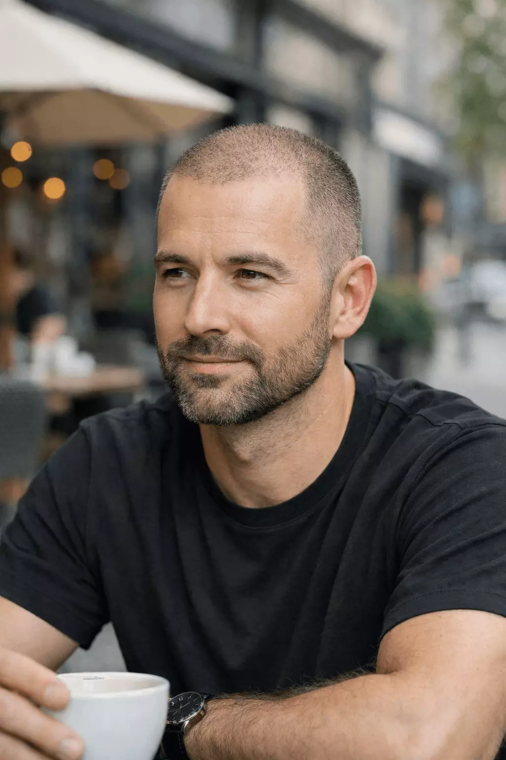 Man with thinning hair wearing buzz cut paired with neatly trimmed beard, confident urban style.