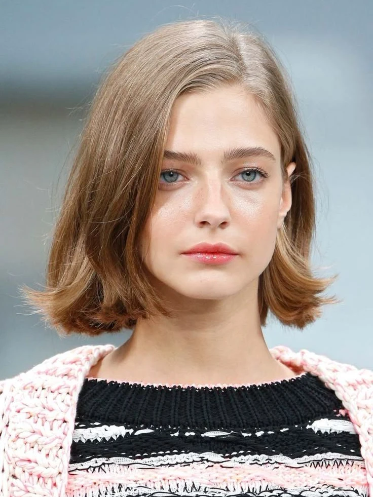 Modern woman with short hairstyle smiling confidently, showcasing clean neckline and fresh haircut highlighting facial features.